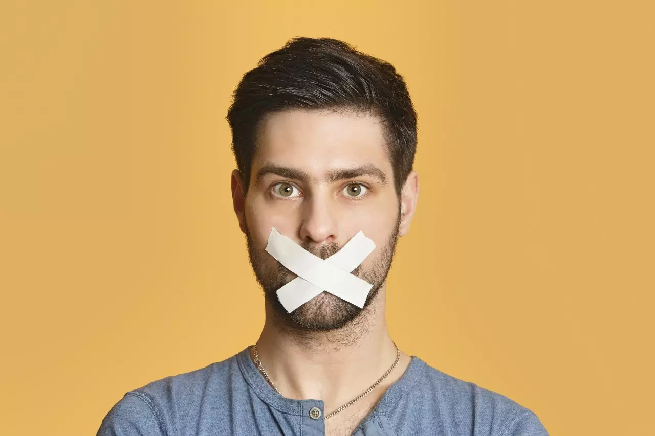 Young adult in front of a colored background with tape over mouth